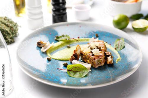 Grilled tuna steak with pistachio nuts, capers and green peas. Tasty dish on a blue plate. Food photography.