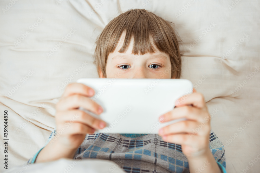 Modern little child lies on bed with smartphone in his hands. Addiction on gadgets concept Modern little child lies on bed with smartphone in his hands. Addiction on gadgets concept
