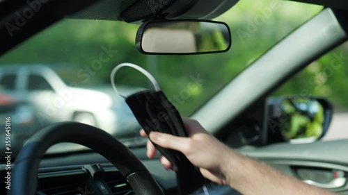 Person hanging black face mask on car rear view mirror. Traveling with protection concept