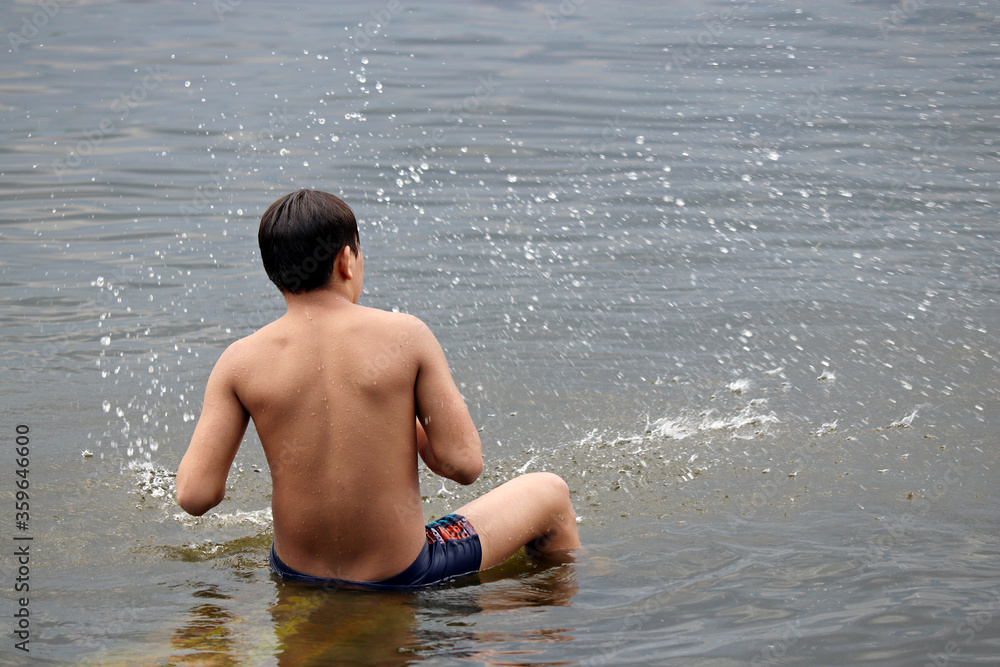 Fototapeta premium Wet guy in trunks splashing in a water. Beach vacation, enjoying the summer