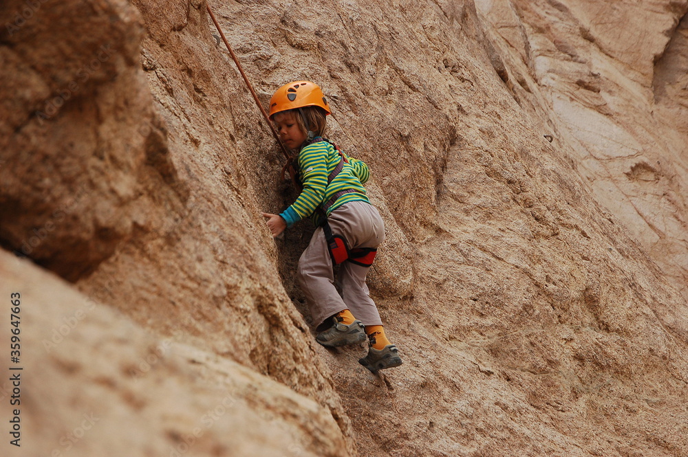 little boy climbs on the rock with rope