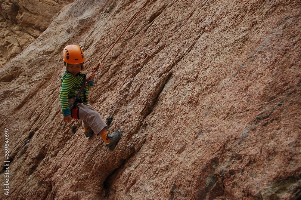 Fototapeta premium little boy climbs on the rock with rope
