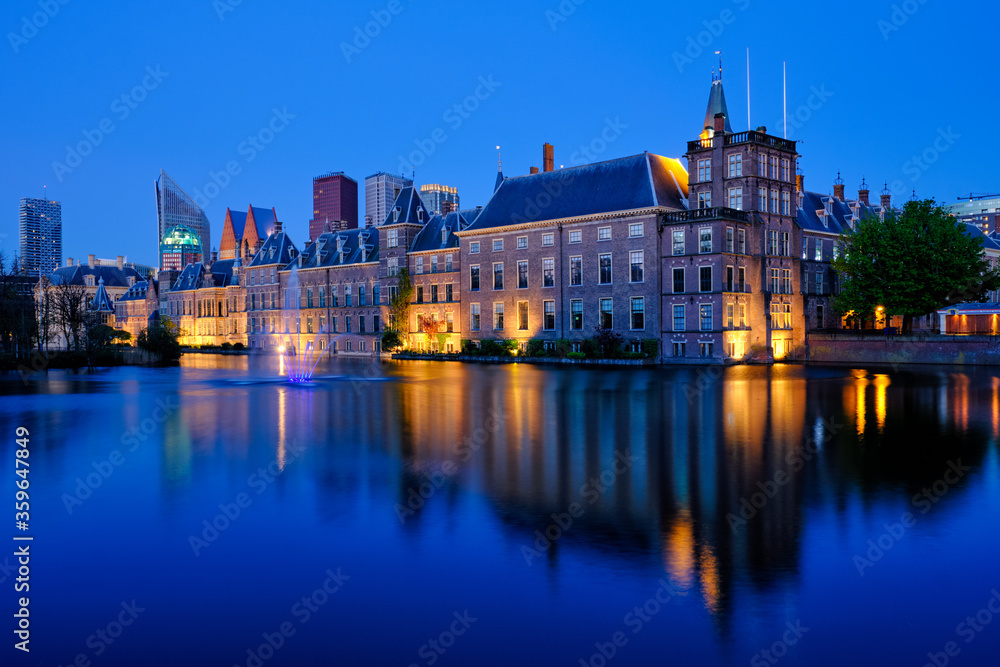 View of the Binnenhof House of Parliament and the Hofvijver lake with downtown skyscrapers in background illuminated in the evening. The Hague, Netherlands