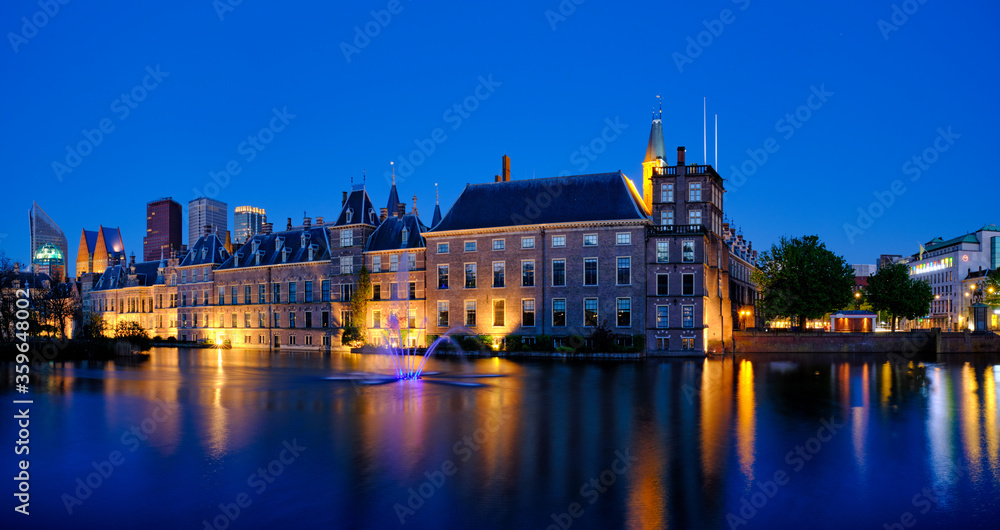 View of the Binnenhof House of Parliament and the Hofvijver lake with downtown skyscrapers in background illuminated in the evening. The Hague, Netherlands View of the Binnenhof House of Parliament and the Hofvijver lake with downtown skyscrapers in background illuminated in the evening. The Hague, Netherlands