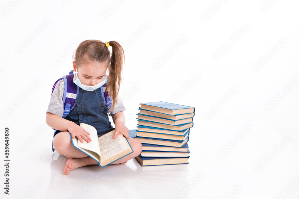 a first-grader learns to read. a little girl on home distance learning. A child in a medical mask reads a book. the student is doing homework. isolated on a white background