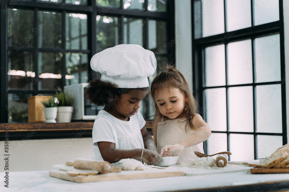 Diverse group of African American and Caucasian girls prepare the dough and bake cookies in the kitchen while learning in the class at school Diverse group of African American and Caucasian girls prepare the dough and bake cookies in the kitchen while learning in the class at school
