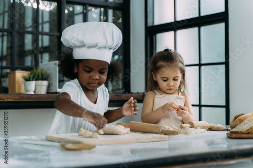 Diverse group of African American and Caucasian girls prepare the dough and bake cookies in the kitchen while learning in the class at school