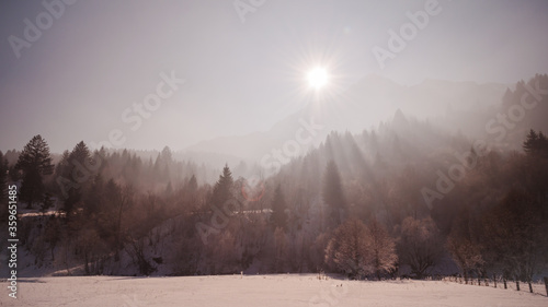 Bright sun over Piatra Craiului mountain with light rays filtred by trees in winter.
