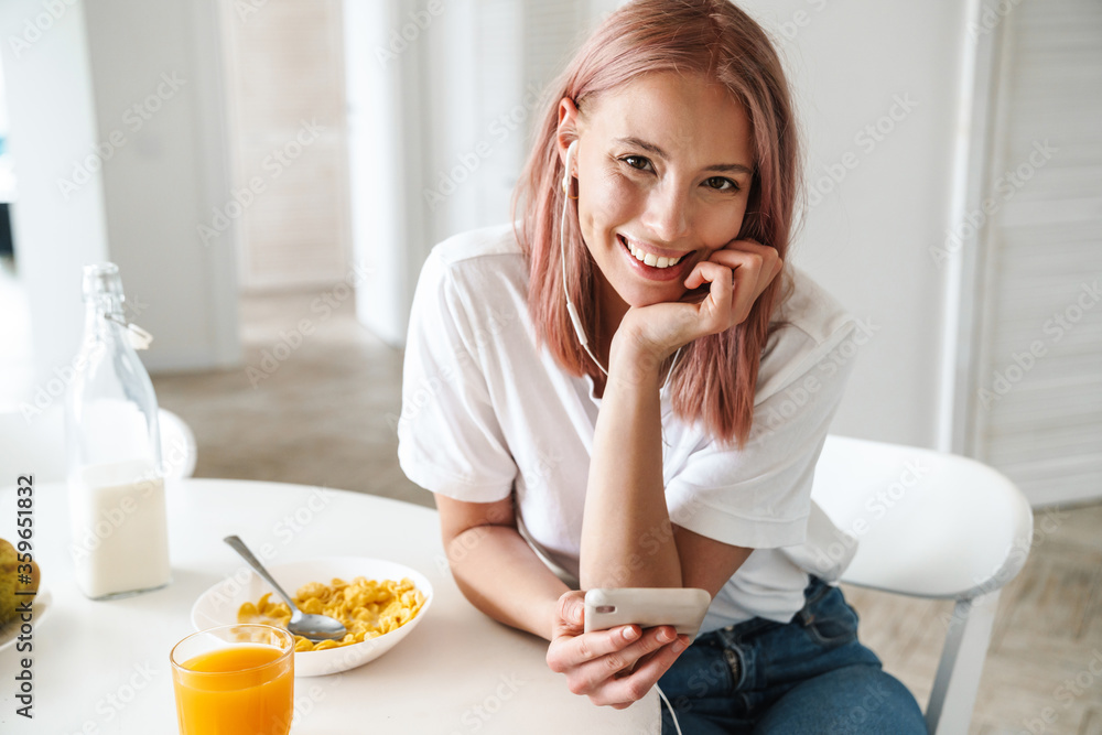 Photo of woman using cellphone and earphones while having breakfast