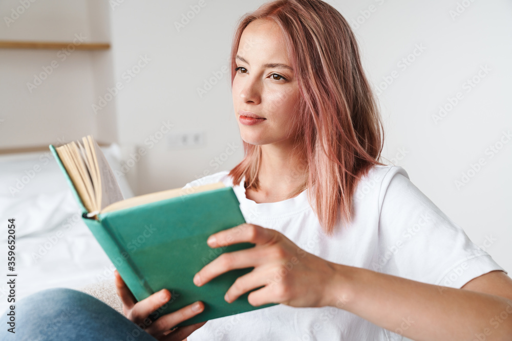 Image of focused pretty woman with pink hair reading book and thinking Image of focused pretty woman with pink hair reading book and thinking