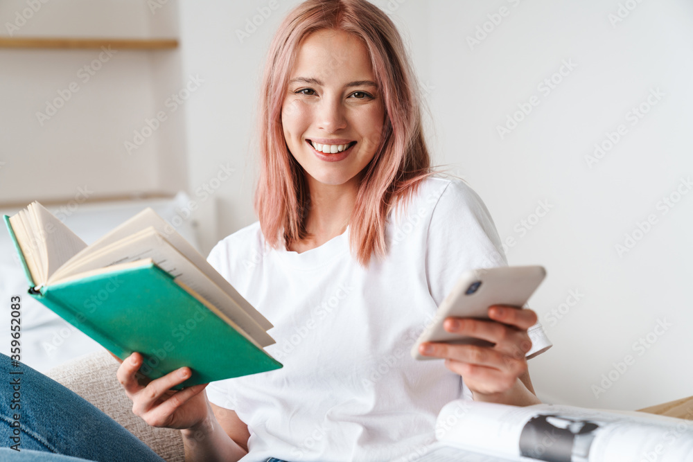 Image of joyful pretty woman reading book and using cellphon Image of joyful pretty woman reading book and using cellphon