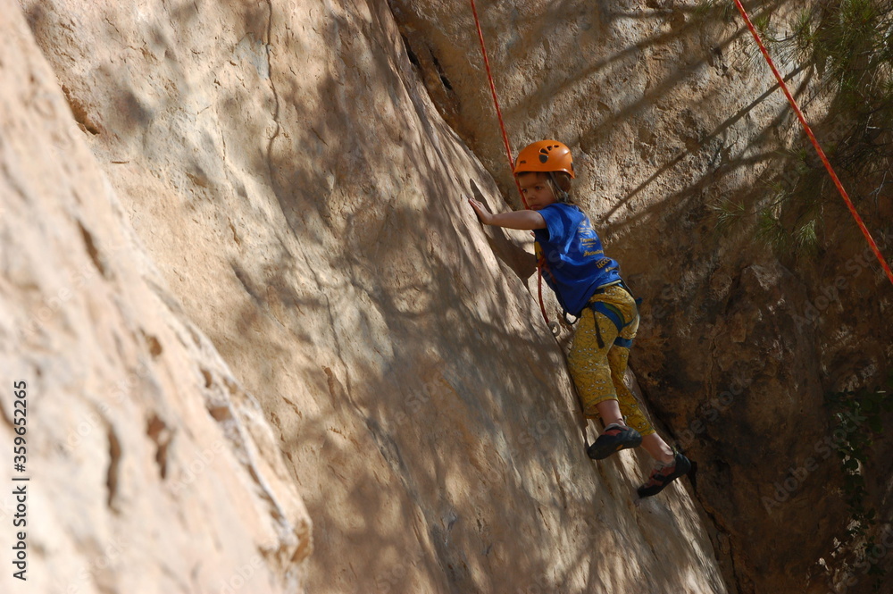 little boy climbs on the rock with rope