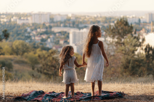 Принти на полотні Two little sisters in white clothes standing on a blanket watching the city whil