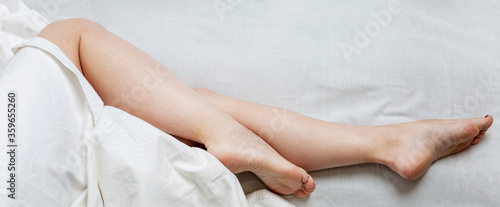 Slender legs of a sleeping woman on the bed. Full sleep and relaxation. Panorama format. Space for text.