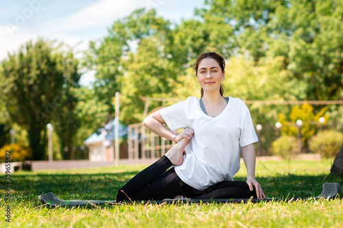 Yoga. A smiling young woman in sports clothes, doing an exercise in the Park on the grass. Side view. The concept of sport for a healthy lifestyle © _KUBE_