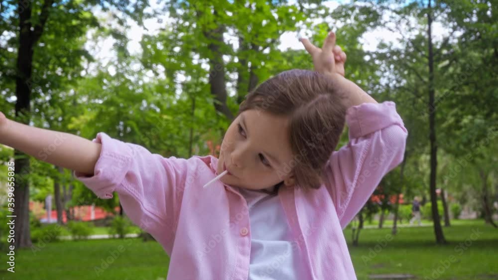 kid with lollipop taking selfie and showing peace sign in park kid with lollipop taking selfie and showing peace sign in park