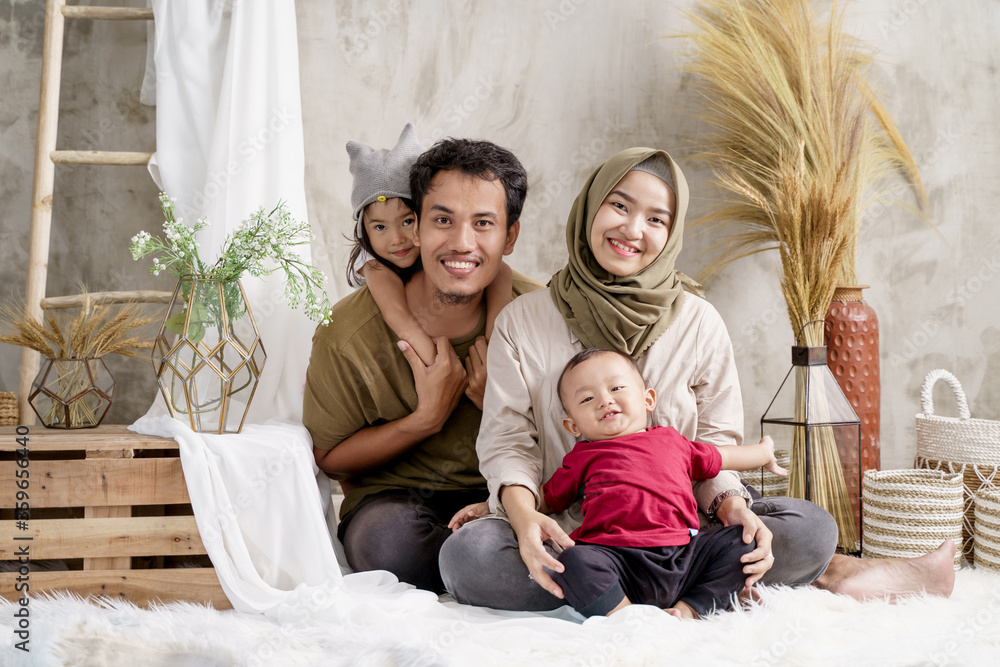 father, mother and two children comfortably sit on the carpet with smile when looking at the camera