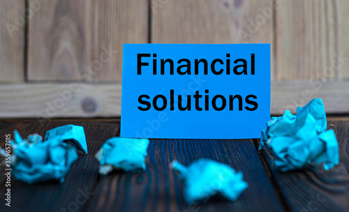 FINANCIAL SOLUTIONS - words on blue paper on a dark wooden background with crumpled pieces of paper photo