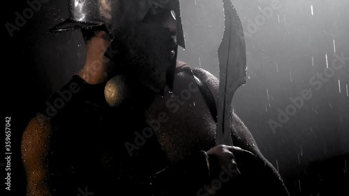 Muscular spartan looking at raindrops on blade.