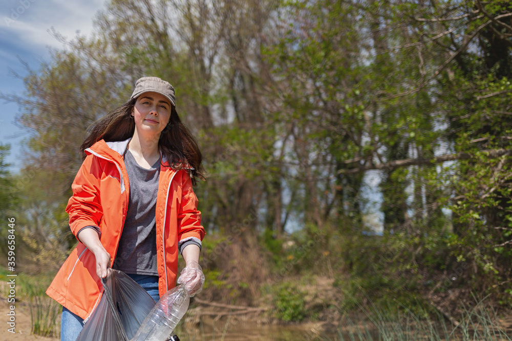 A female volunteer smiles and collects garbage in the Park area. The concept of the protection of the environment and Earth Day