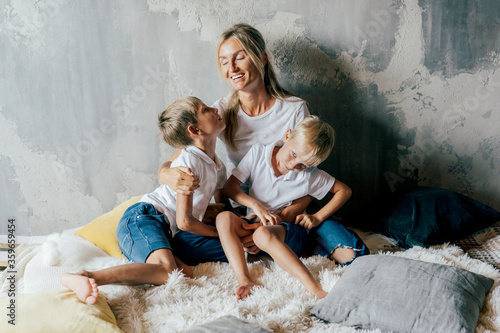 Beautiful white young mother hugs her sons in bed. Family time. Lifestyle portrait. Sharing time.