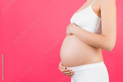 Close up of pregnant belly at pink background. Mother is wearing white underwear and holding her abdomen. Parenthood concept. Copy space © sosiukin