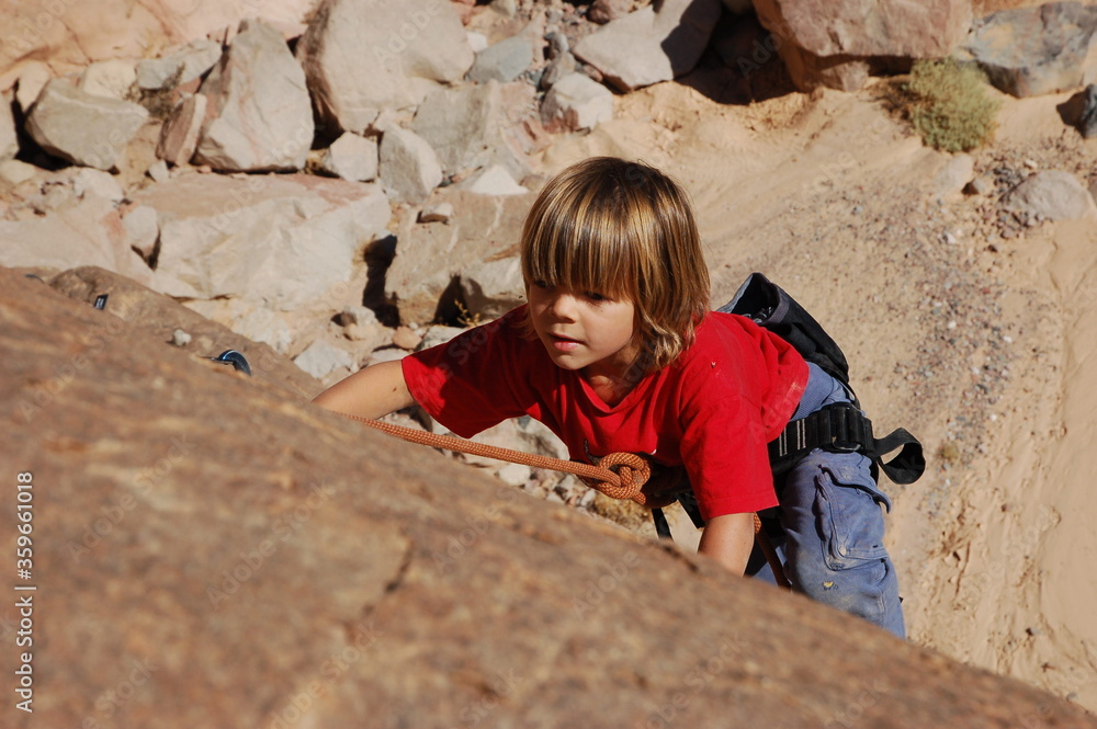 little boy climbs on the rock with rope