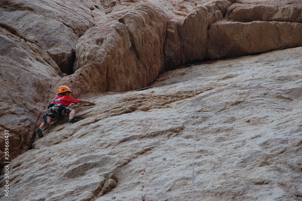 little boy climbs on the rock with rope