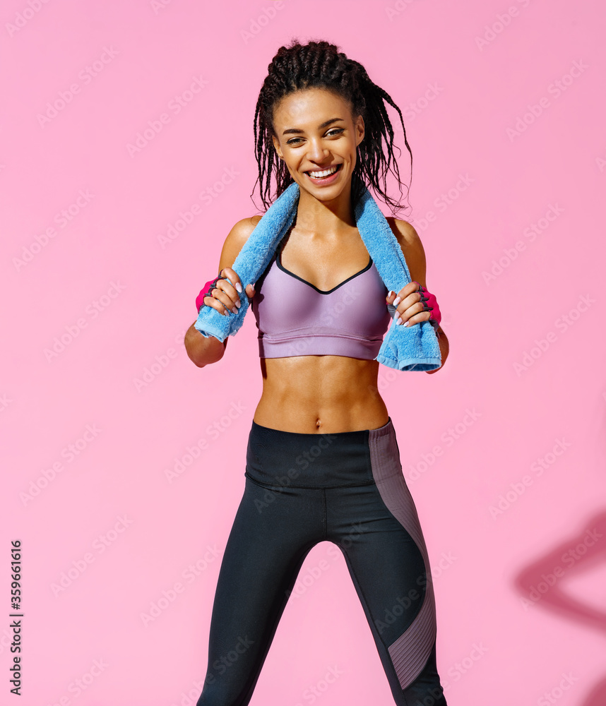 Resting time. Sporty girl with towel after training. Photo of african american girl with perfect body on pink background. Strength and motivation Resting time. Sporty girl with towel after training. Photo of african american girl with perfect body on pink background. Strength and motivation