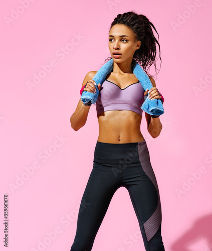 Resting time. Sporty girl with towel after training. Photo of african american girl with perfect body on pink background. Strength and motivation