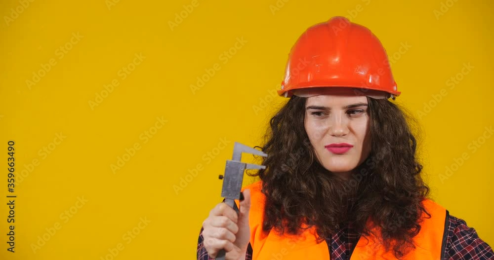 Attractive plus-size model posing. Curly-haired brunette on bright yellow studio background. Girl in red helmet and orange signal vest showing large size with caliper. Erotic Fantasy Concept Attractive plus-size model posing. Curly-haired brunette on bright yellow studio background. Girl in red helmet and orange signal vest showing large size with caliper. Erotic Fantasy Concept