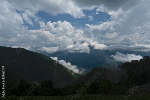 Panorama of the mountains of the Caucasus. Clouds over the rocky peaks. Snow on the rocks. Fog in the valleys after a rainstorm.