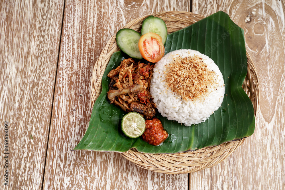 ayam geprek with white rice and sliced of tomato, cucumber, lime and sambal served on a traditional woven plate,Indonesian cuisine concept