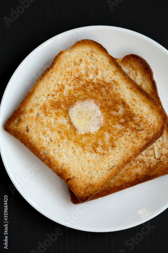 Homemade Buttered Toast on a white plate on a black background, top view. Flat lay, overhead, from above.