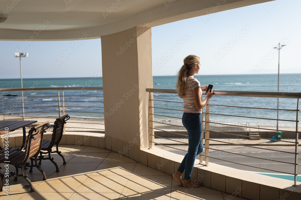 Caucasian woman standing on a balcony holding a smartphone and taking a selfie Caucasian woman standing on a balcony holding a smartphone and taking a selfie