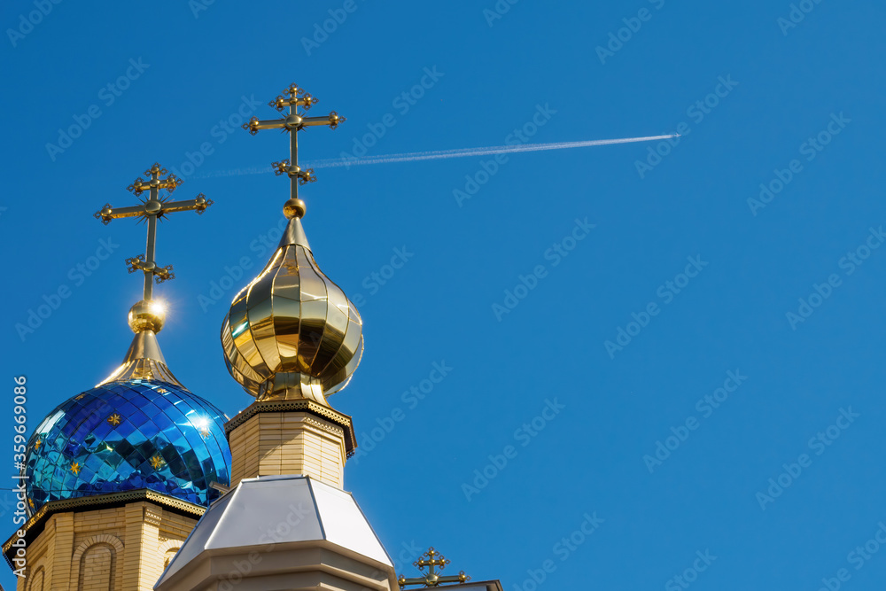 Domes of the temple with crosses against blue sky and flying plane with white trace. Orthodox church and flying airplane