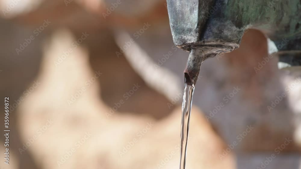 Flowing drinking water of an ancient fountain with moving shadows in the blurred background Flowing drinking water of an ancient fountain with moving shadows in the blurred background