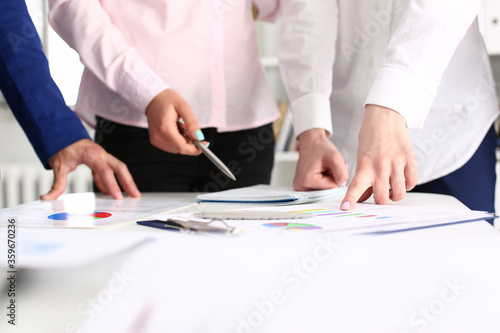 Close up of young woman holding pen and pointing at graphic while standing by the table with coworkers