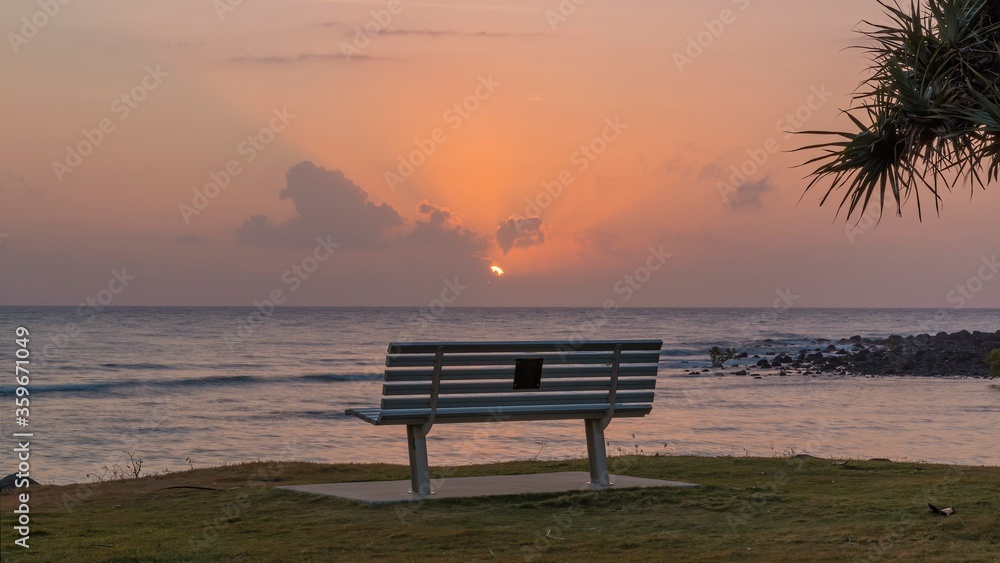 A bench remains empty as the sun rises over the Coral Sea