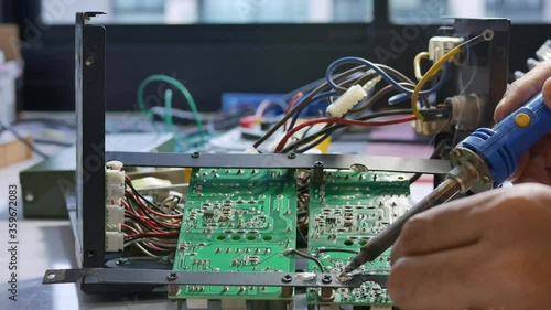 Electronic technician is soldering the electric wires to the motherboard of an electronic device.