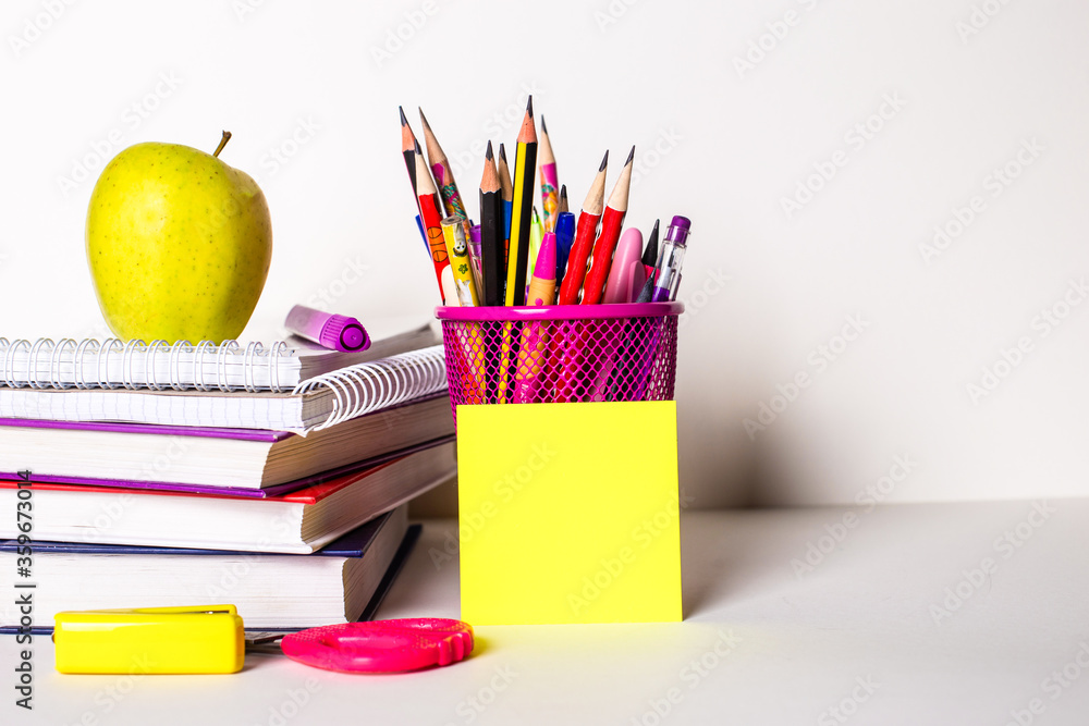 Naklejka premium On a light background, textbooks, stationery, a sticker and an apple. School concept