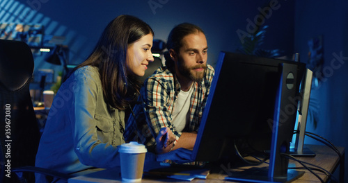 Picture of professional video editors editing video on computer with two displays in modern video studio. Young man and woman talking about project