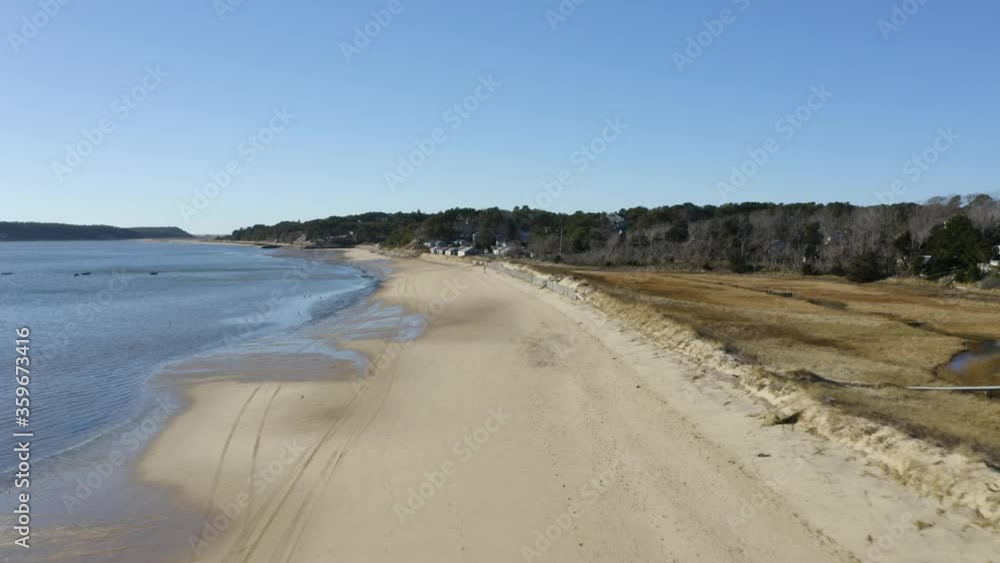 The camera flys up Mayo beach in Wellfleet harbor. You can see the town cottages and various coastal homes that are on the shoreline. There are various shore birds along the shoreline during low tide The camera flys up Mayo beach in Wellfleet harbor. You can see the town cottages and various coastal homes that are on the shoreline. There are various shore birds along the shoreline during low tide
