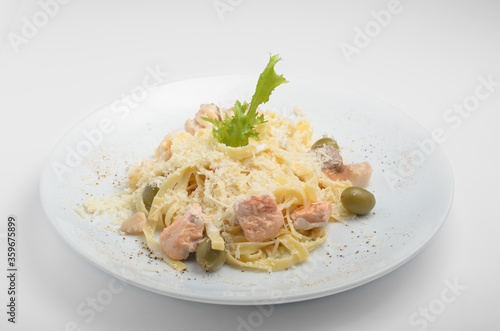 Tagliatelle pasta with seafood, olives, arugula and grated parmesan cheese. Beautifully served on a white plate, shot on a white background. For use in the online menu