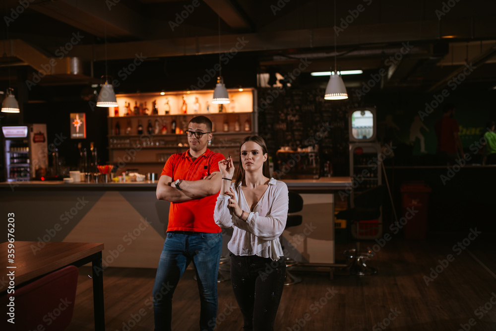 Portrait of a beautiful caucasian  girl throwing an arrow on a dart board, while behind her stands a man in a red T-shirt