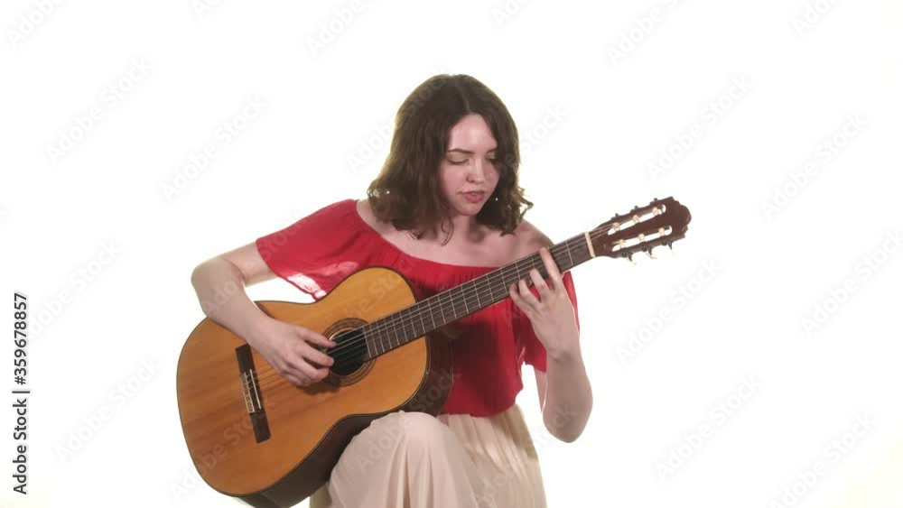 young girl musician in a red blouse playing the classical acoustic guitar. Medium long shot. Closeup. Isolated young girl musician in a red blouse playing the classical acoustic guitar. Medium long shot. Closeup. Isolated