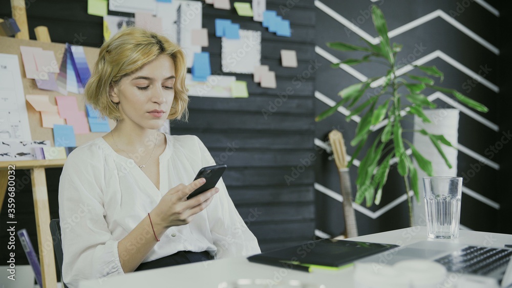 Young woman designer working uses phone on the table Young woman designer working uses phone on the table