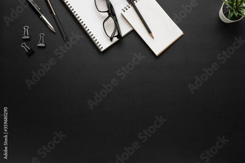 Top view above of black office desk table with notebook, pen and coffee cup, glasses with equipment other office supplies. Business and finance concept. Flat lay with blank copy space.