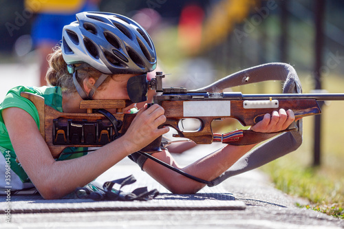 Young girl aiming rifle on biathlon shooting range photo