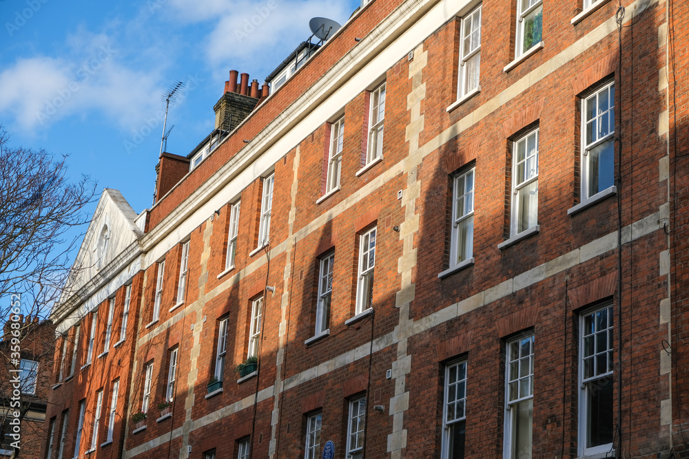 A row of red brick buildings partly covered in shadows in London